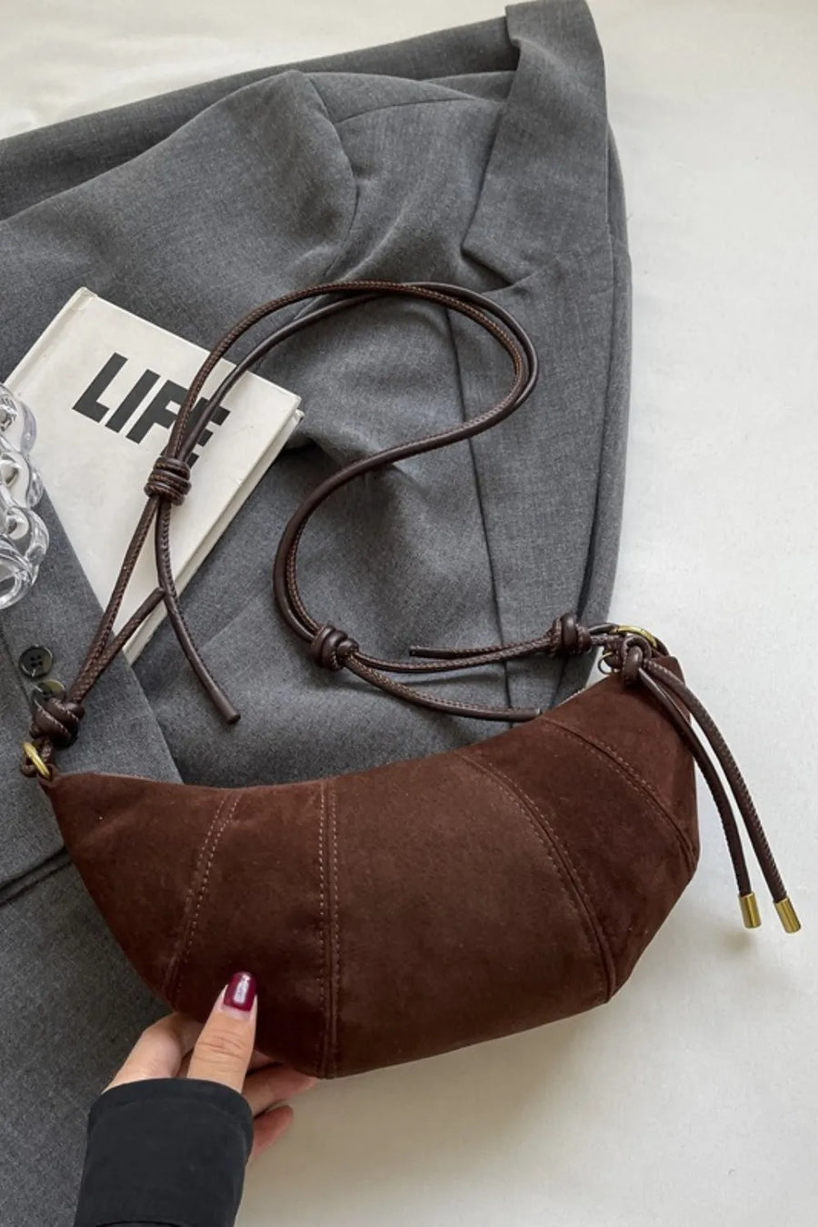 Brown suede crescent shoulder bag with knot detail and gold hardware.