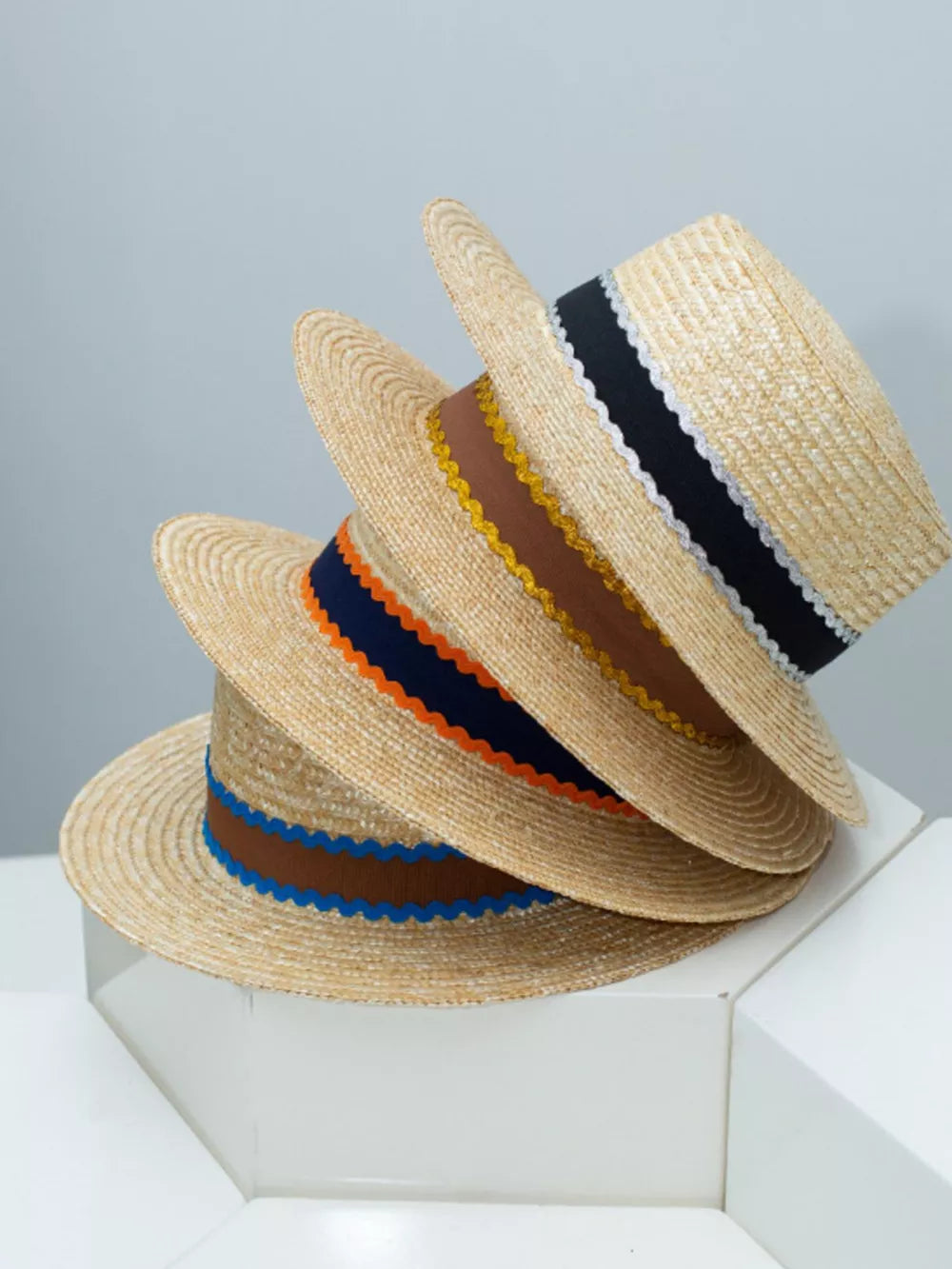 Straw boater hats stacked with decorative bands in blue, orange-red, and navy.