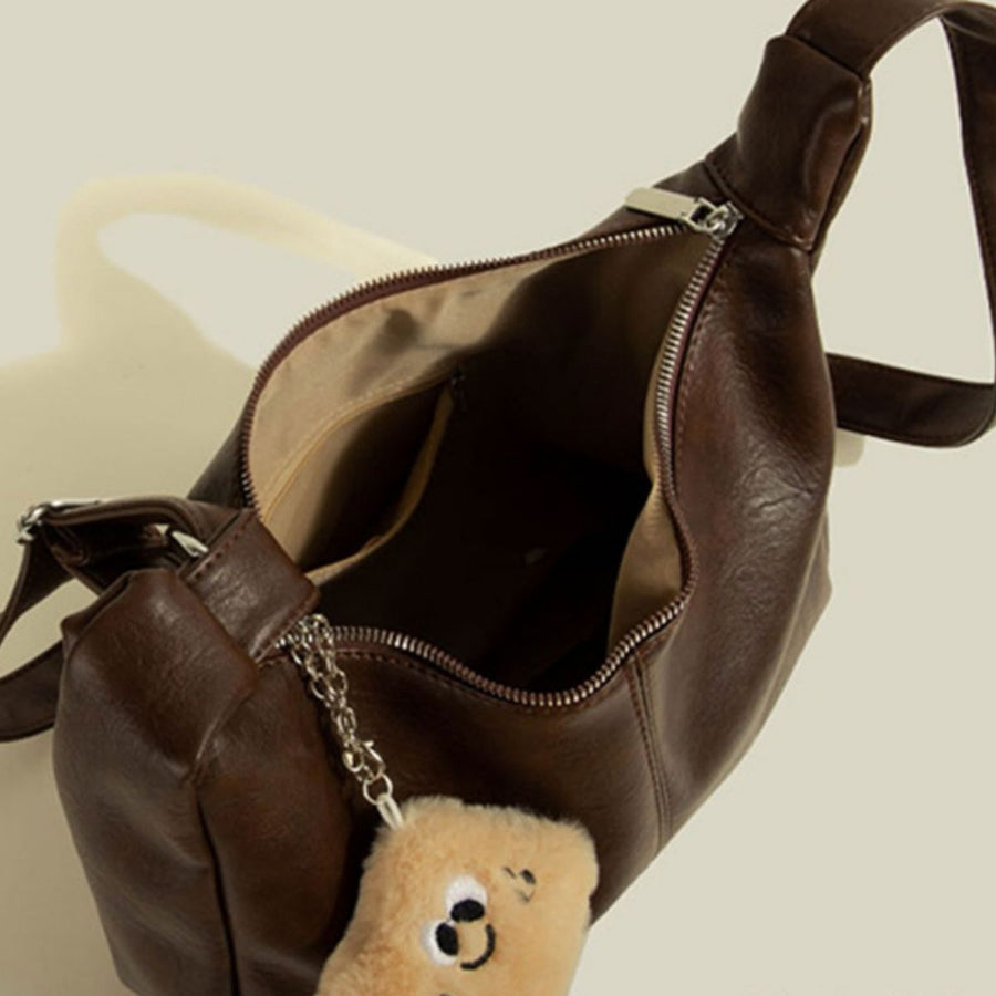 Brown crescent shoulder bag made of pu leather with a fluffy bear charm.