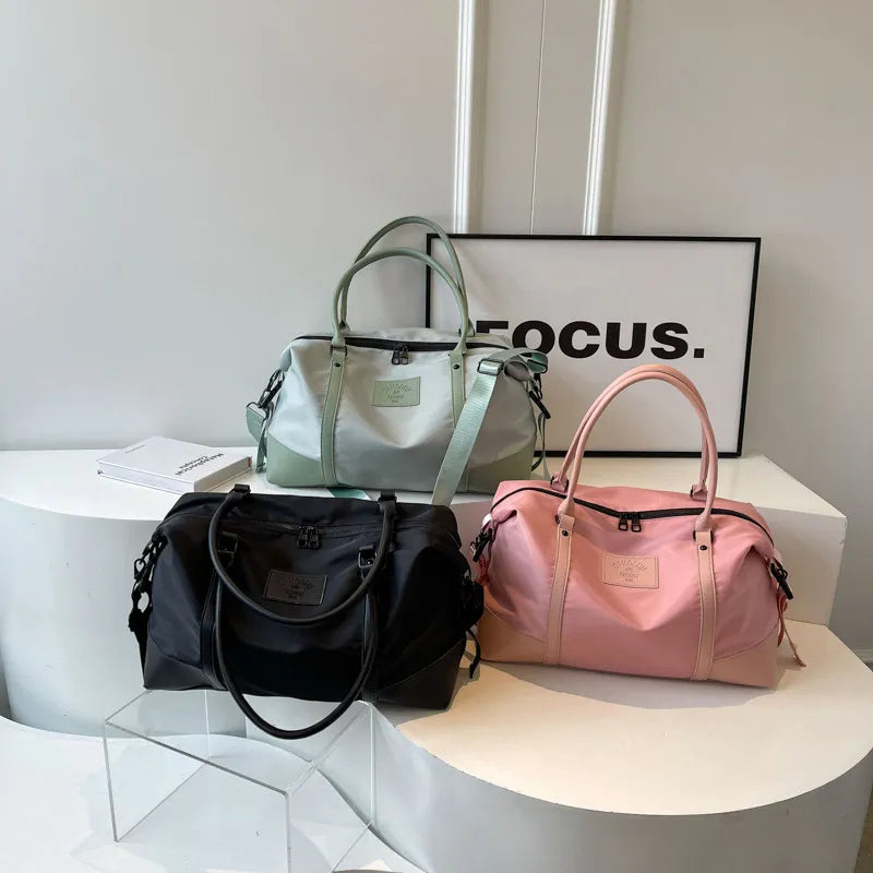 Duffel bags in blush pink, sage green, and black with top handles and shoulder straps.