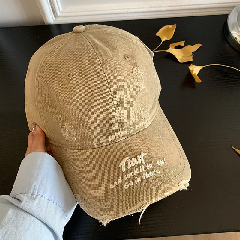 Distressed tan baseball cap with embroidered text and frayed details