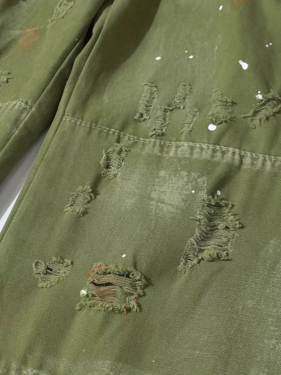 Olive green cargo pants with distressed rips and paint splatters.