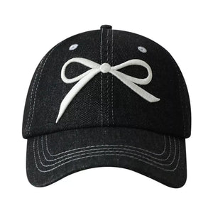 Black baseball cap with white embroidered bow accent and contrast stitching.