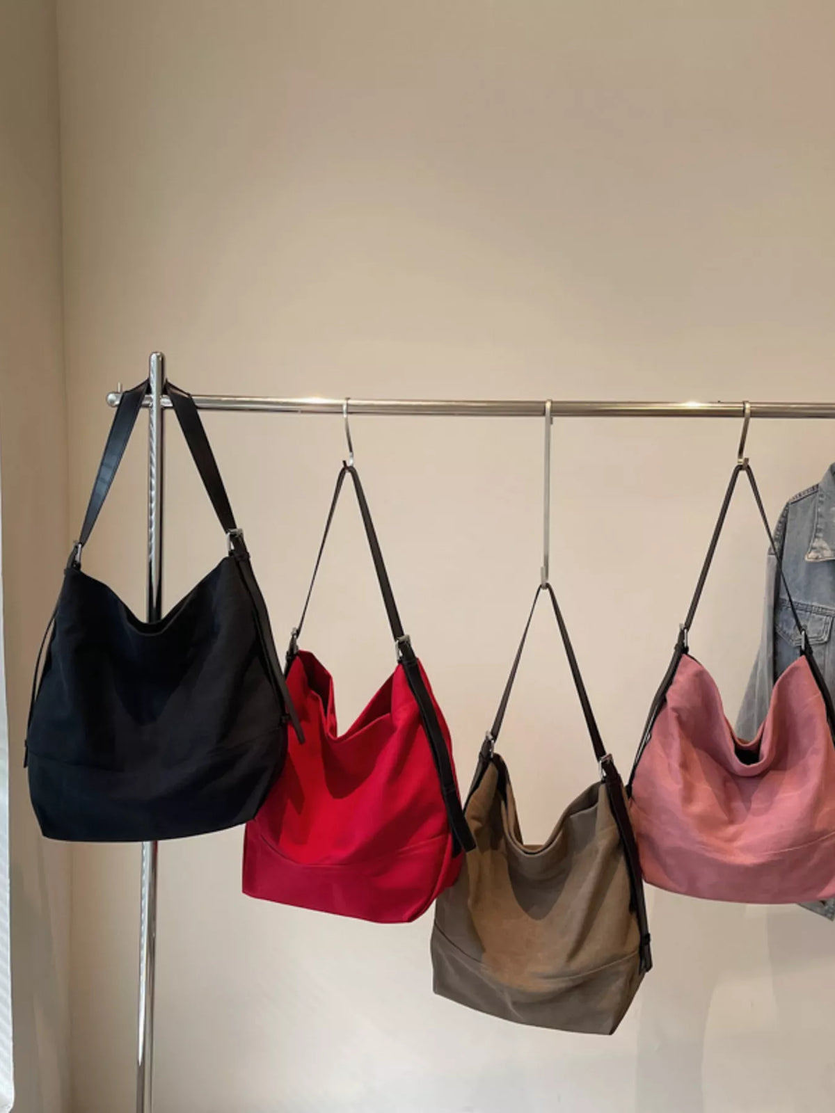 Black, red, brown, and pink hobo bags with adjustable straps hang on a rack.