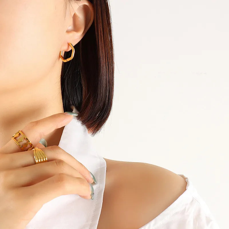 Gold Sharp Triangle geometric steel huggie earrings on ear, styled with gold rings.