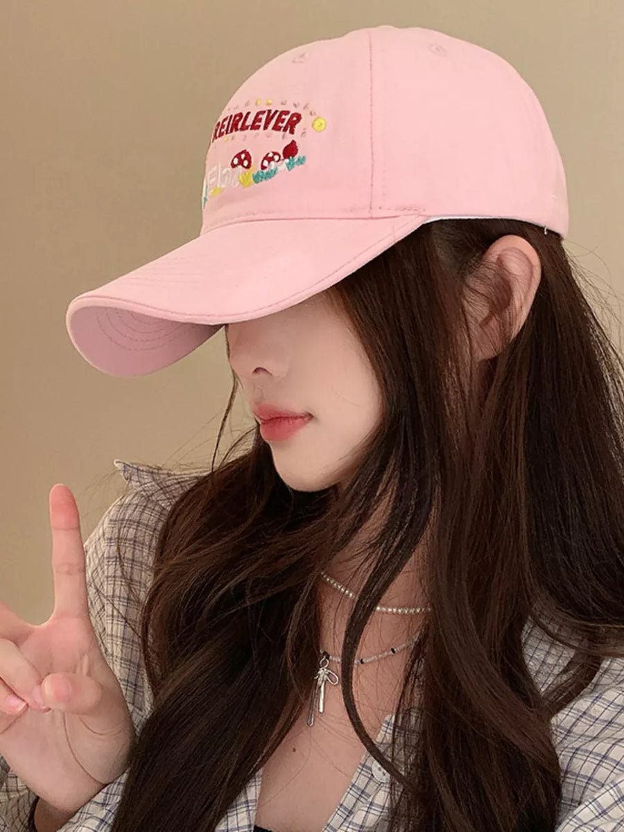 Blush pink baseball cap with playful mushroom embroidery and text detail.