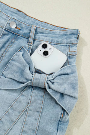 Light wash denim shorts with a large bow detail on the pocket.