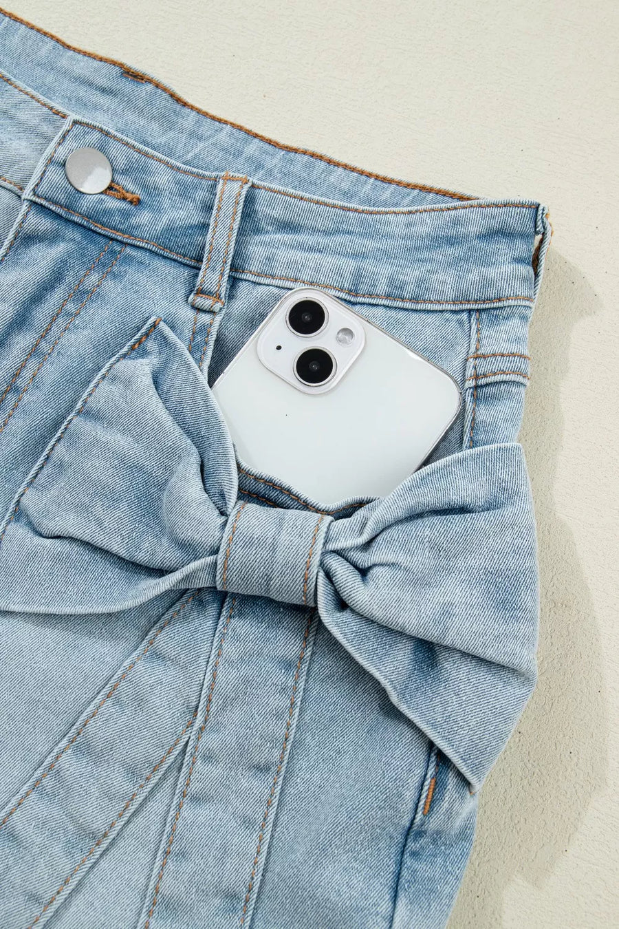 Light wash denim shorts with a large bow detail on the pocket.