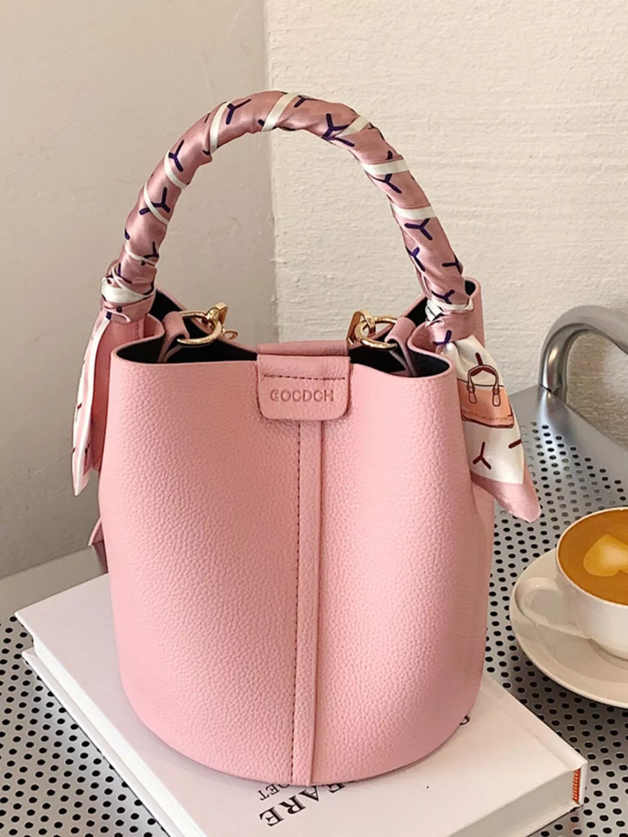 Pink bucket crossbody bag with decorative scarf on handle