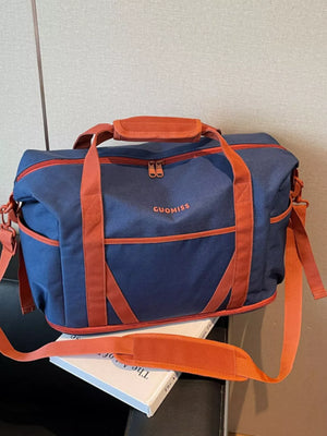 Duffel bag in navy blue with orange trim and straps, featuring a top handle and adjustable shoulder strap.