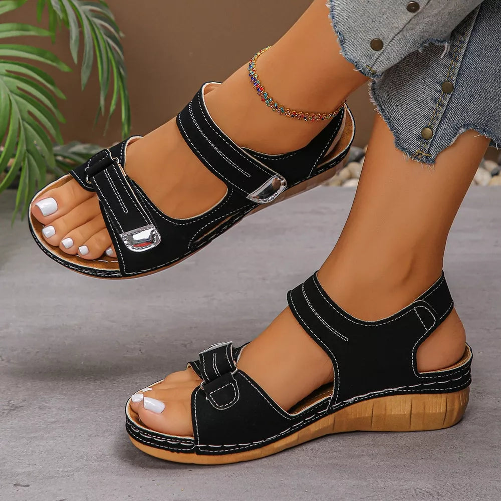 Black adjustable wedge sandals with white stitching and silver buckle details.