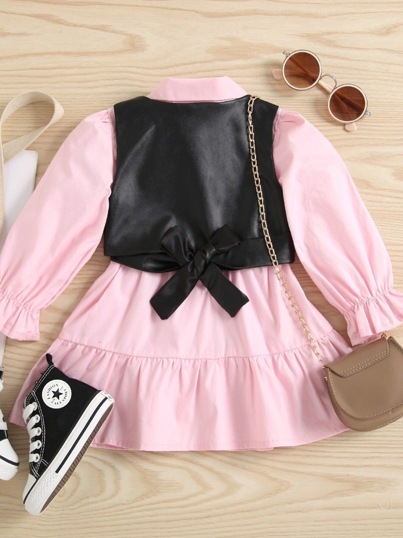 Toddler pink cotton dress with black faux leather vest, bow detail, and ruffled sleeves.