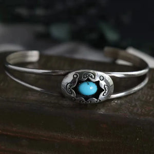 Turquoise cabochon open bangle bracelet with ornate silver setting.