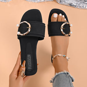 Black open-toe slide sandals with pearl and gold buckle detail.