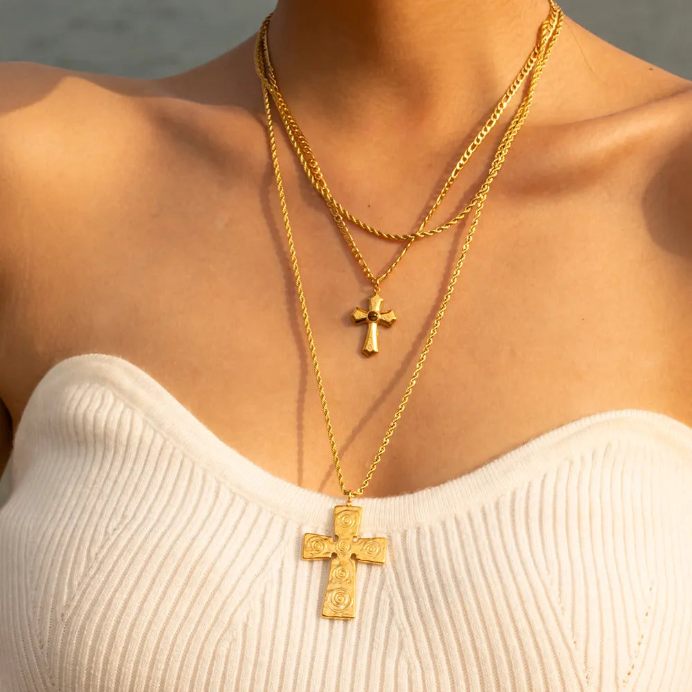 Gold layered chain necklaces with sculpted cross pendants, one with intricate swirl detail.