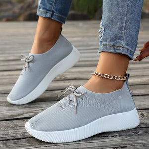 Gray lace-up sneakers with white mid sole and textured knit upper.