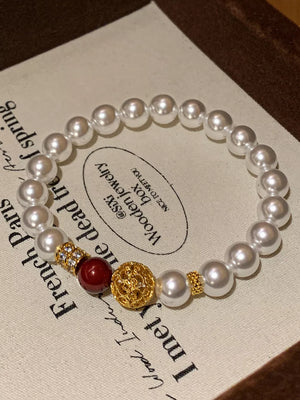 Elegant pearl beaded bracelet with gold accents and a red bead.