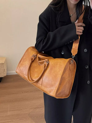 Cognac vintage leather duffle bag with top handles and adjustable shoulder strap.