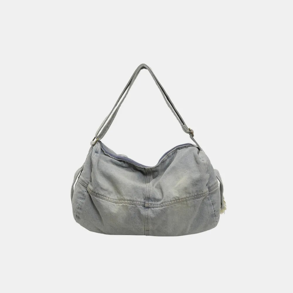 Washed denim hobo bag in light blue with adjustable strap and zippered top.