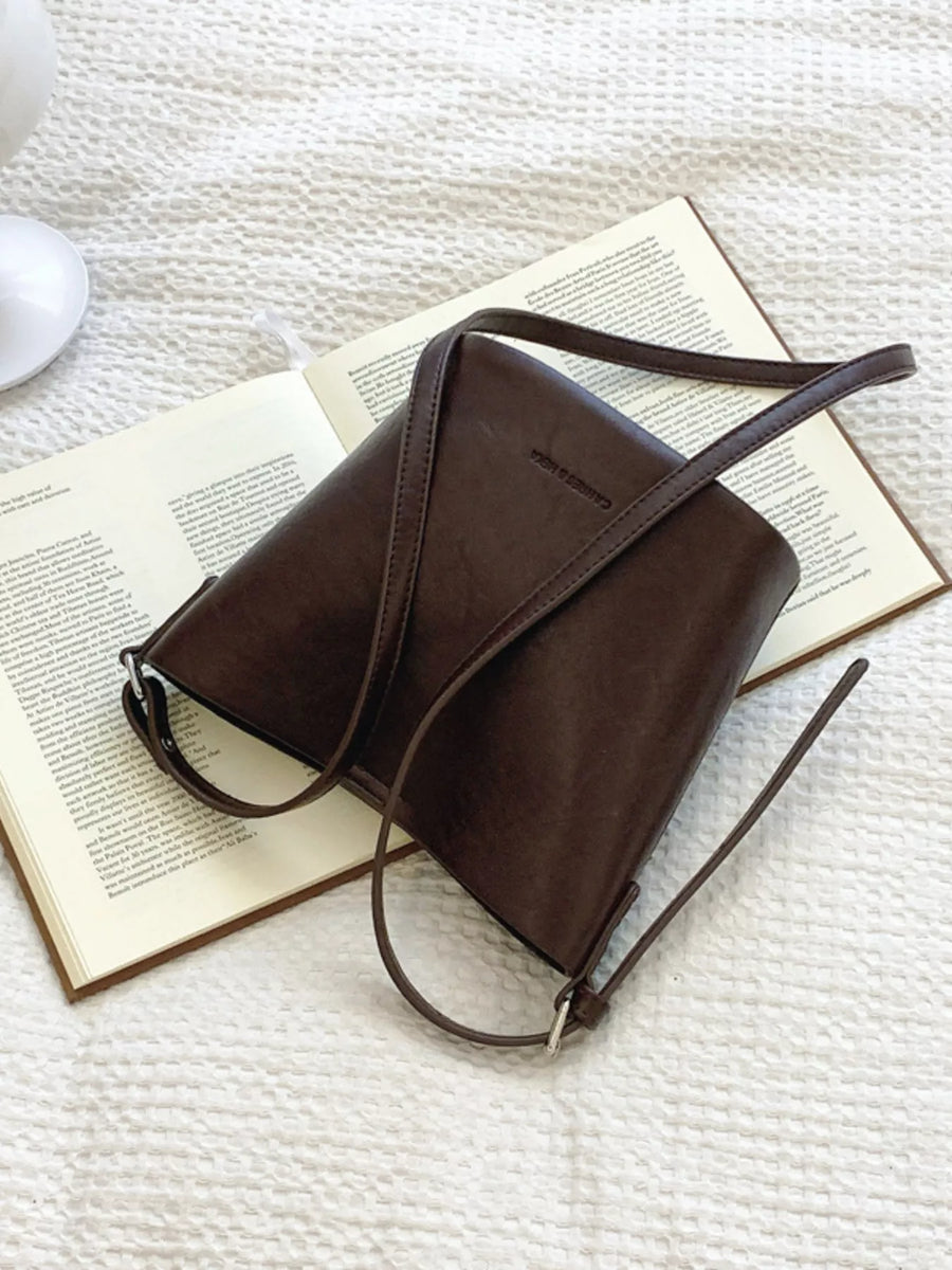 Sleek leather bucket crossbody bag in chocolate with adjustable strap.