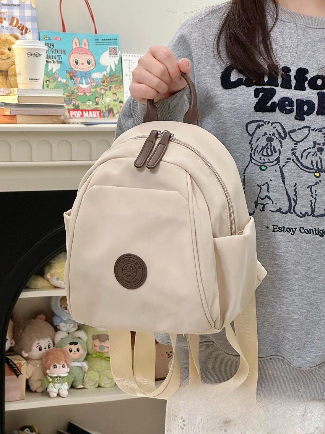 Cream nylon mini backpack with zippered pockets and a bear patch detail.