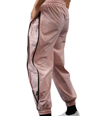 Dusty pink track pants with full-length side zippers and reflective logo detail.