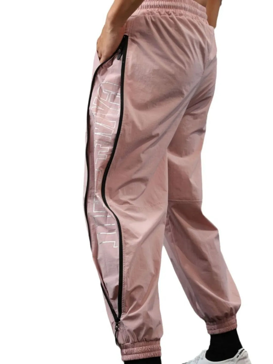 Dusty pink track pants with full-length side zippers and reflective logo detail.