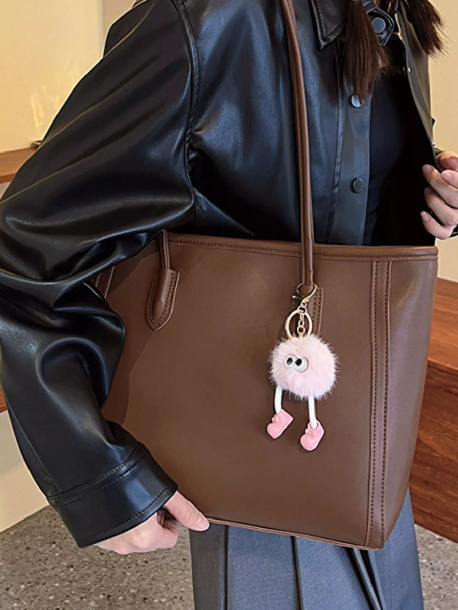 Brown PU leather tote bag with a cute pink pompom charm and a black jacket.