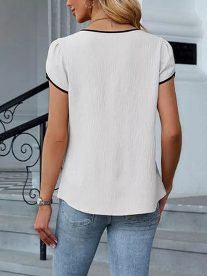 White blouse with black trim, petal sleeves, and textured fabric.