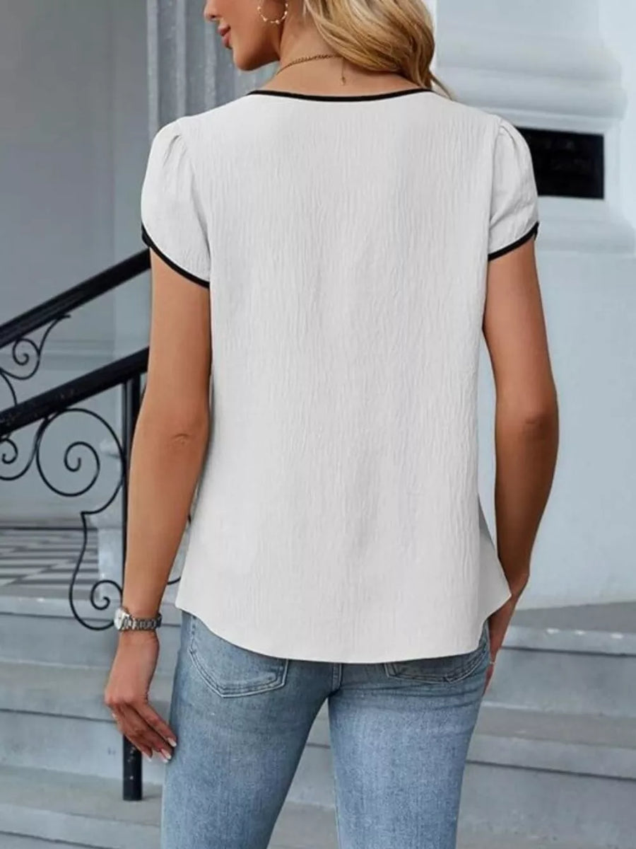 White blouse with black trim, petal sleeves, and textured fabric.