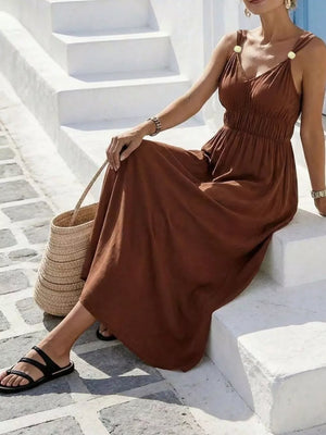 Brown V-neck sleeveless maxi dress with smocked waist and gold button straps.