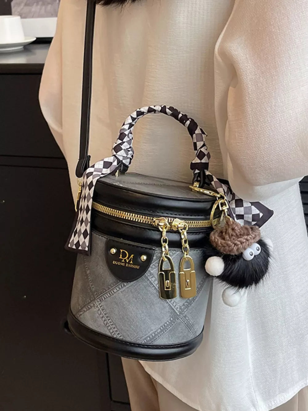 Quilted mini bucket bag in grey with black trim, checkered scarf detail and fuzzy charm.