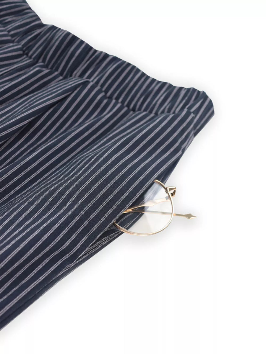 Blue striped wide-leg pants with elastic waistband and pocket detail, showing gold-rimmed glasses.