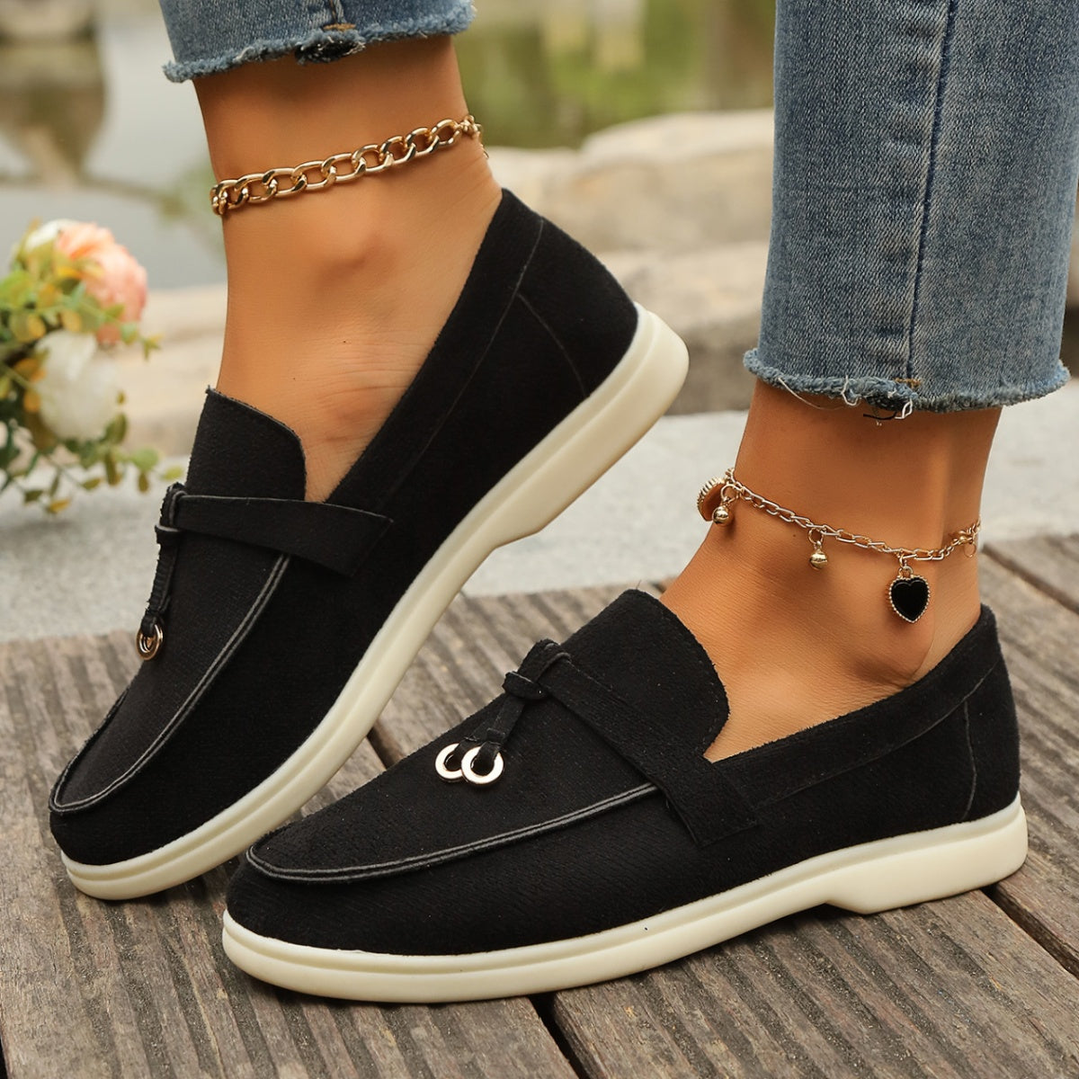 Black decorative strap flat slip-ons with white soles and gold hardware detail.