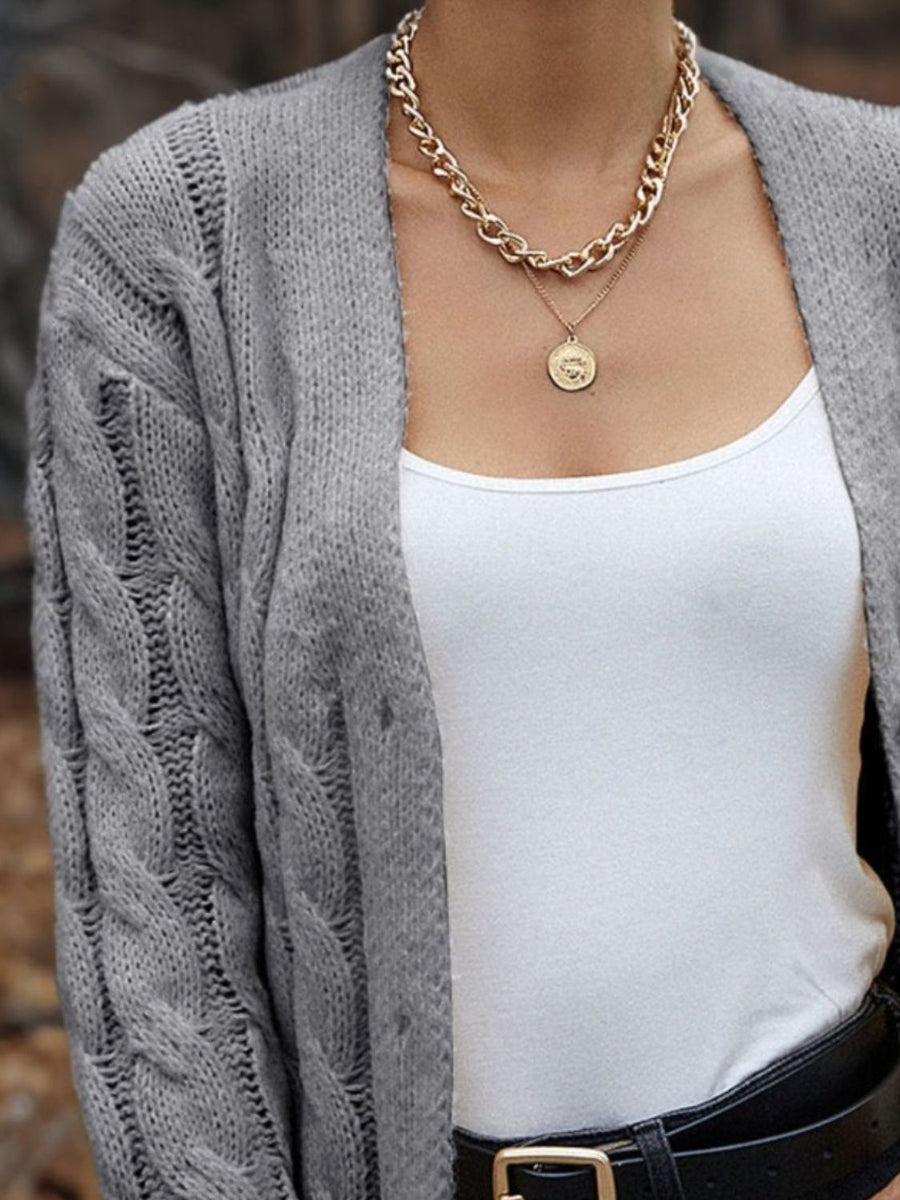 Gray cable knit sleeve cardigan with open front, worn over a white tank top and black belt.