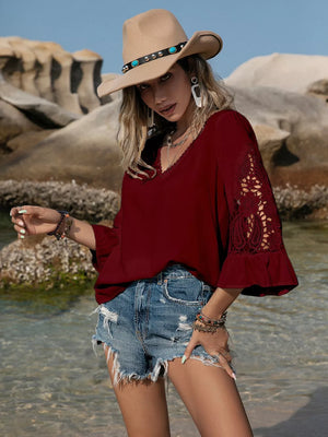 Burgundy V-neck blouse with lace bell sleeves and cutout detail, styled with denim shorts.