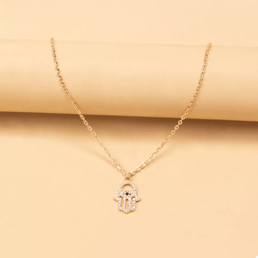 Gold evil eye hamsa pendant necklace with clear rhinestones and black eye detail.