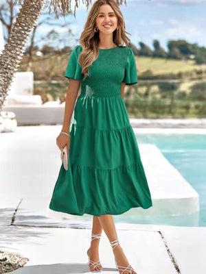 Green smocked tiered midi dress with flutter sleeves and a round neckline.