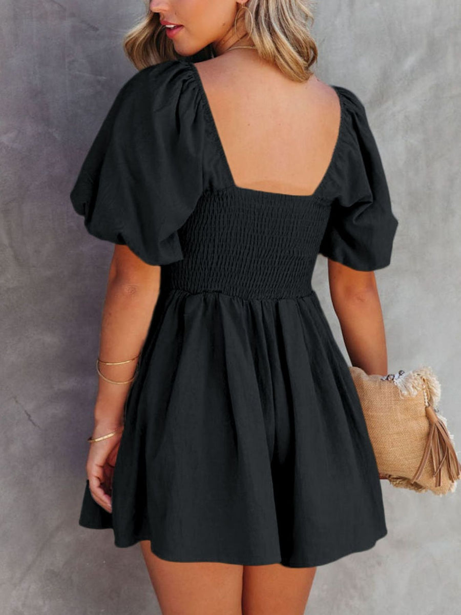 Black ruched puff sleeve square neck cotton romper with smocked bodice and flared skirt.