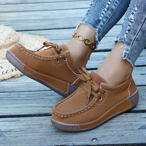Brown suede moccasin style sneakers with white stitching and lace-up detail.