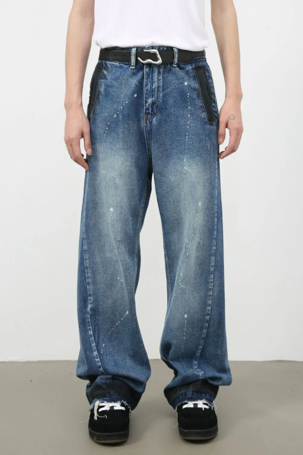 Panelled denim palazzo trousers in medium wash with paint splatters and black leather accents.