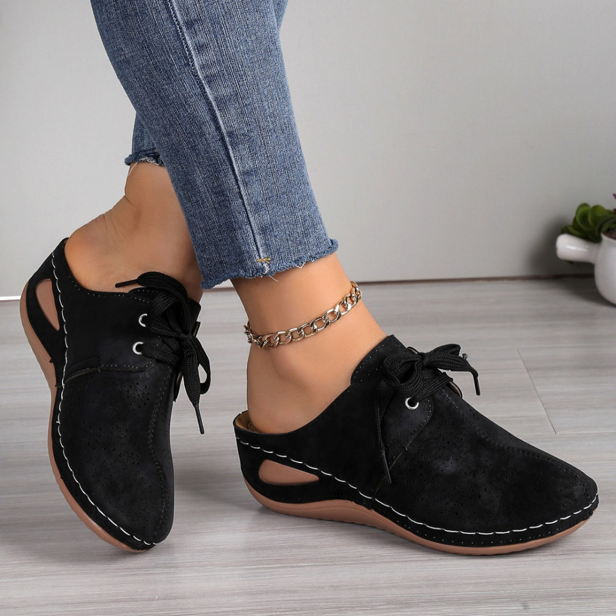 Black perforated slip-on mules with lace-up detail and white stitching.