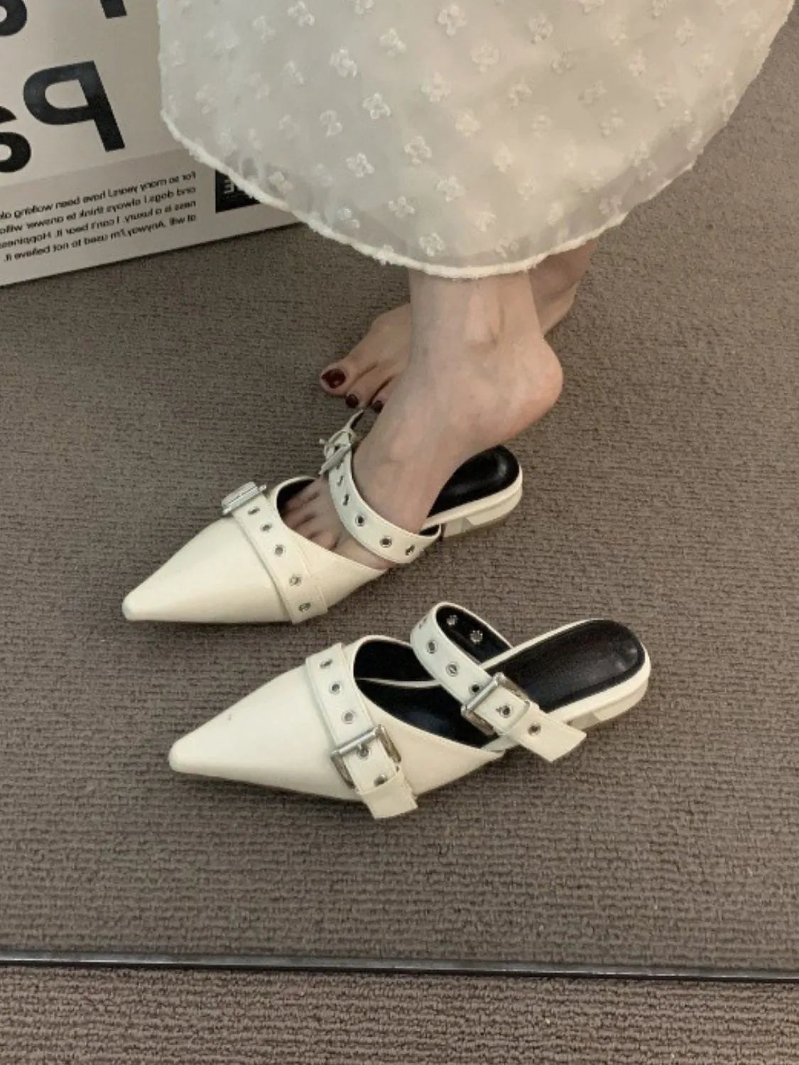 Beige pointed mules with buckle strap detail and silver hardware.