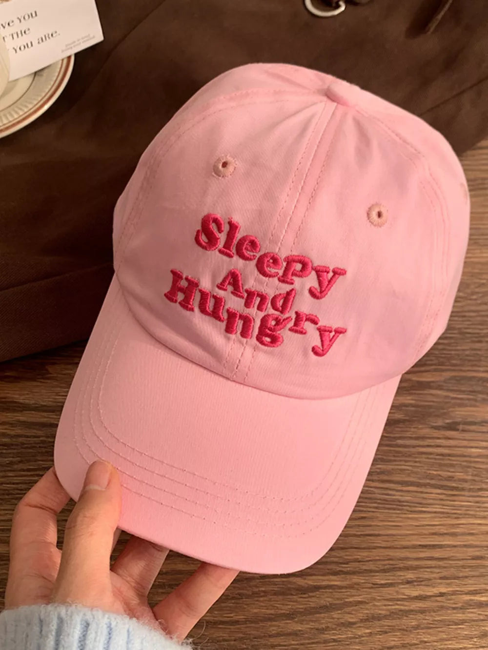 Pink cotton baseball cap with embroidered "Sleepy And Hungry" text.