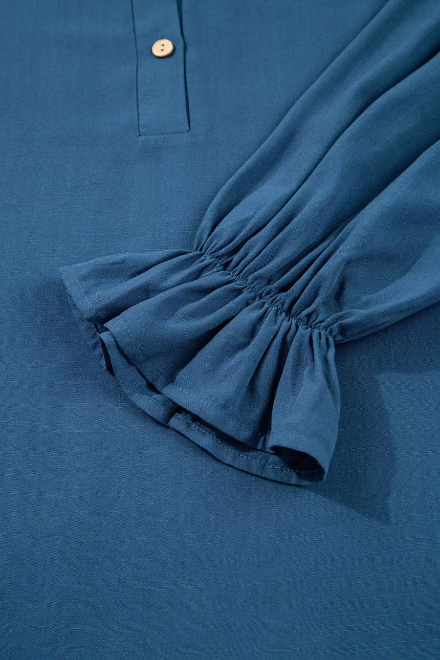 Blue long sleeve blouse with ruffled cuffs and a single button detail