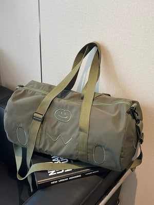 Green duffel bag with embroidered smiley face and adjustable strap.