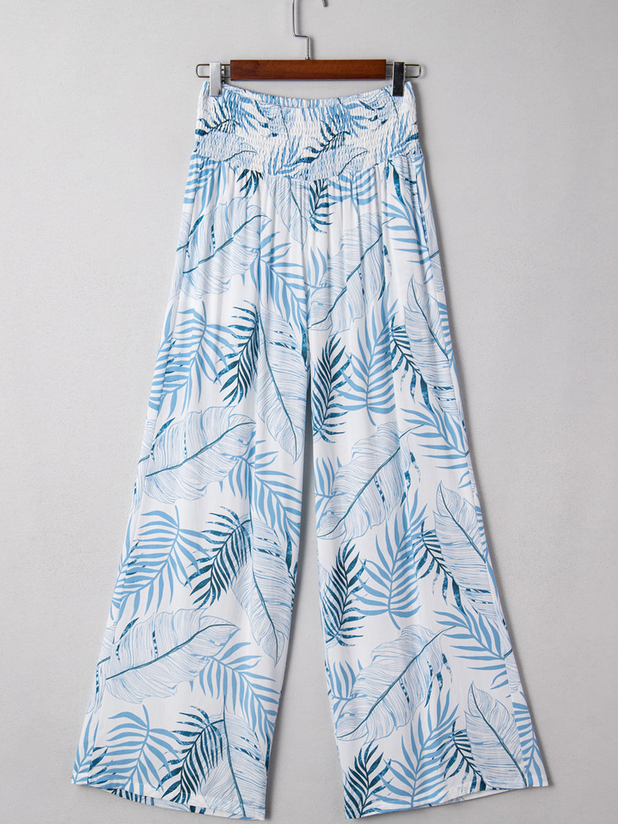 White cotton wide leg pants with blue tropical leaf print and smocked waistband.