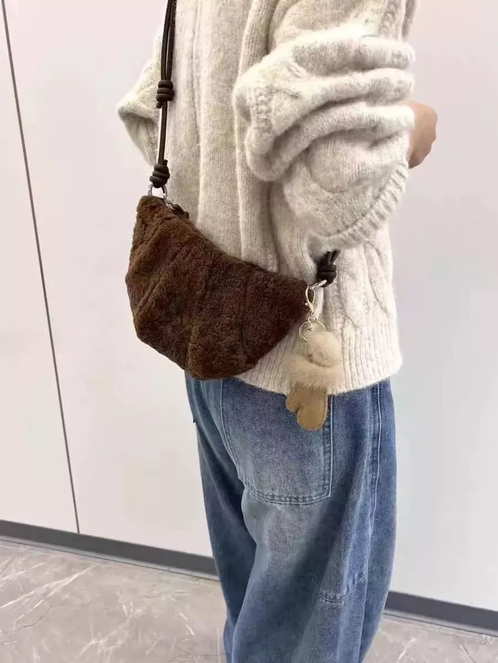 Brown plush knot strap furry crossbody bag with charm, worn casually.