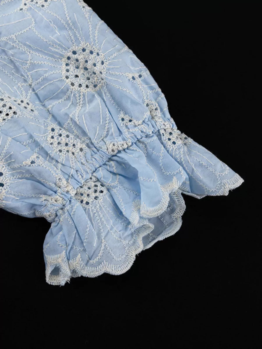 Blue eyelet cotton blouse with ruffled cuffs and floral embroidery.