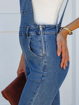 Flared denim overalls in medium wash with a zip front and raw hem detail.